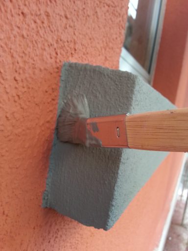 Pensel som målar en grå yta på en orange vägg.